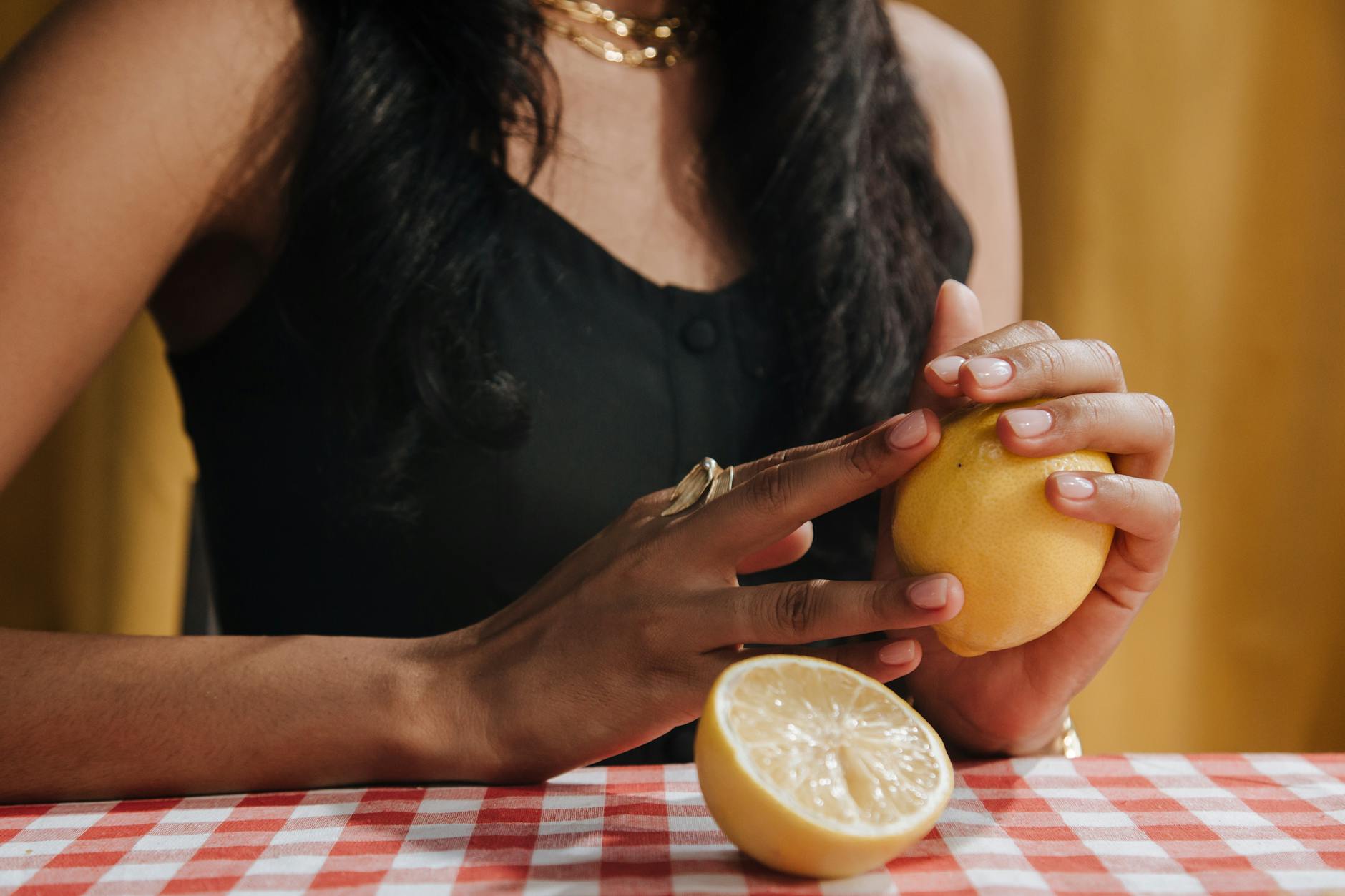 A woman holding a fresh lemon at a dining table, symbolizing wellness and intentional self-care during stressful times.