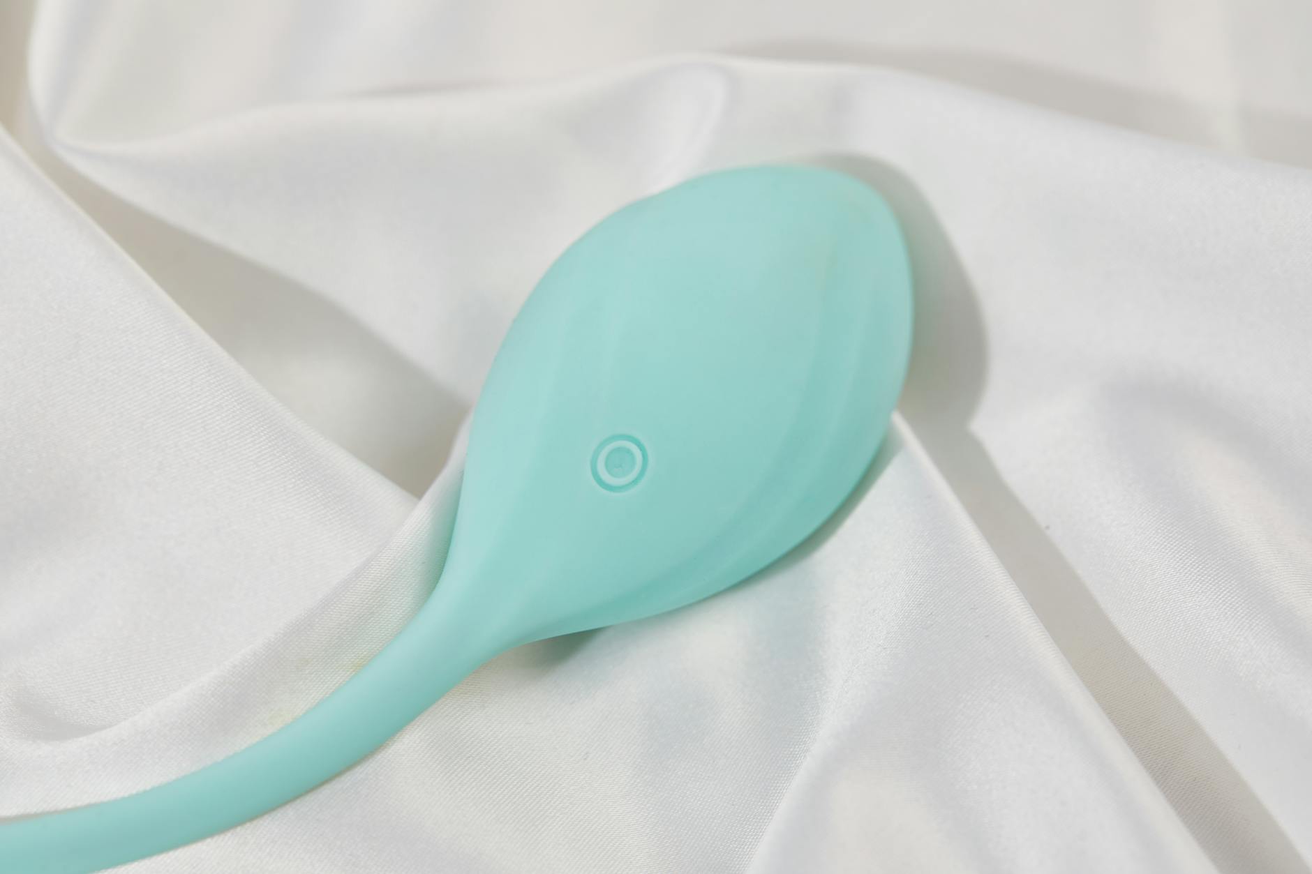 A sleek teal clitoral vibrator resting on soft white silk fabric