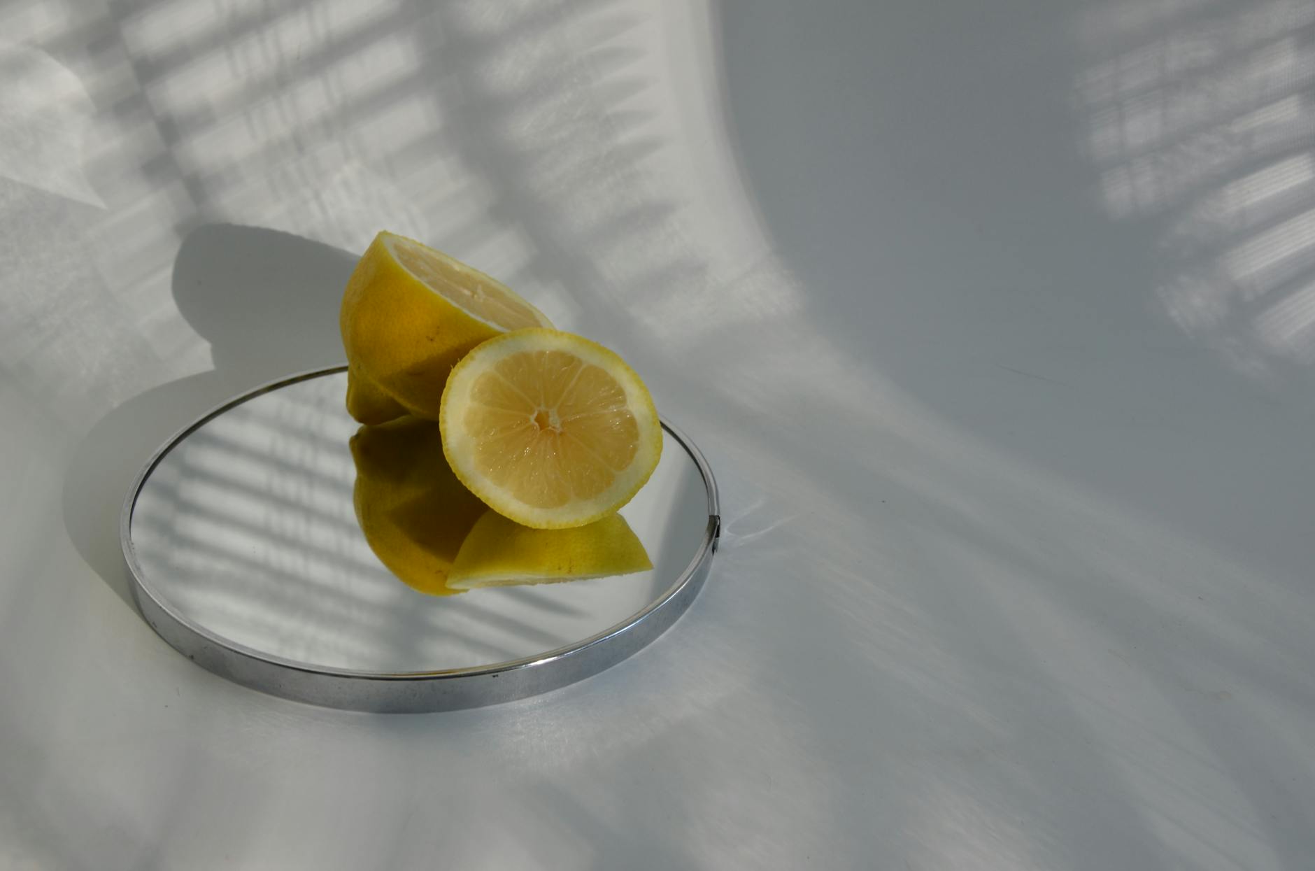 Sliced lemons on a mirror casting shadows, showcasing minimalistic food photography.