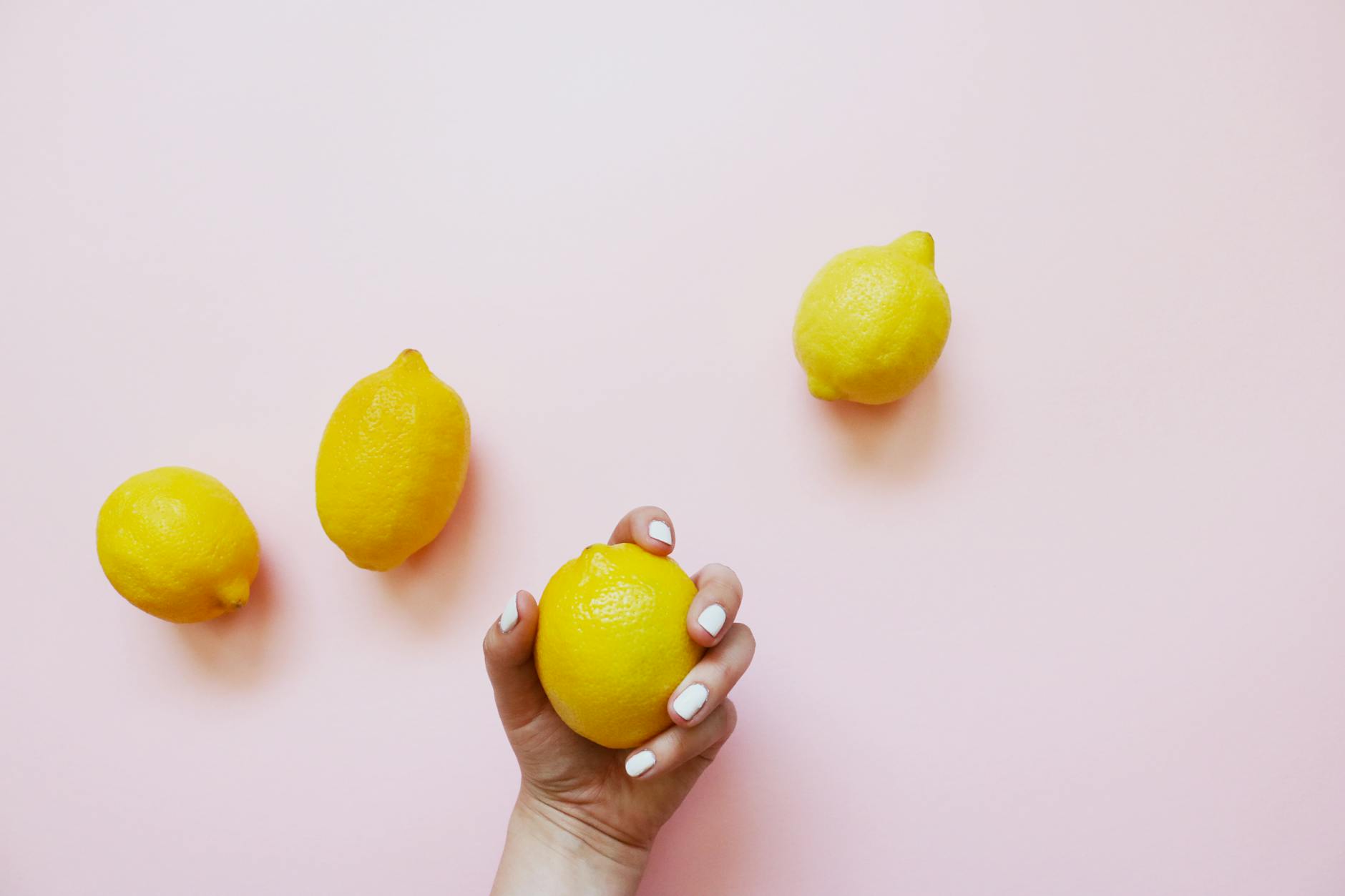 A hand with white nails holding a fresh lemon on a soft pink background, symbolizing the vibrant sexuality of women over 35