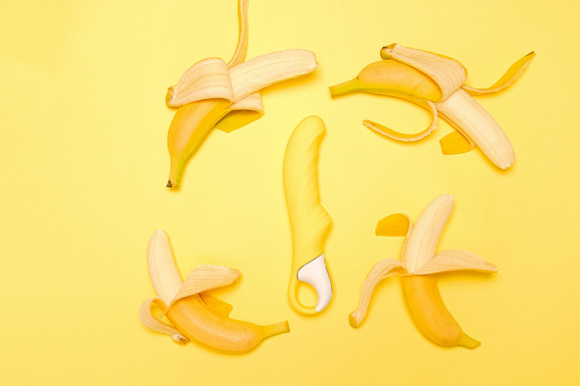 A bright yellow lemon clitoral vibrator surrounded by fresh lemons on a soft yellow surface