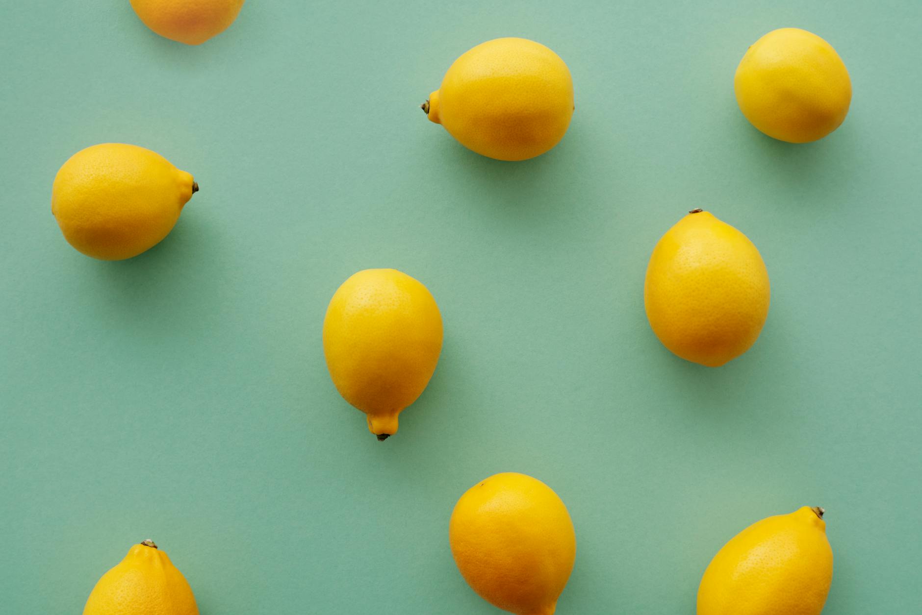 Fresh yellow lemons arranged on a pastel green background, symbolizing the citrus-inspired design of Hello Nancy's clitoral vibrators