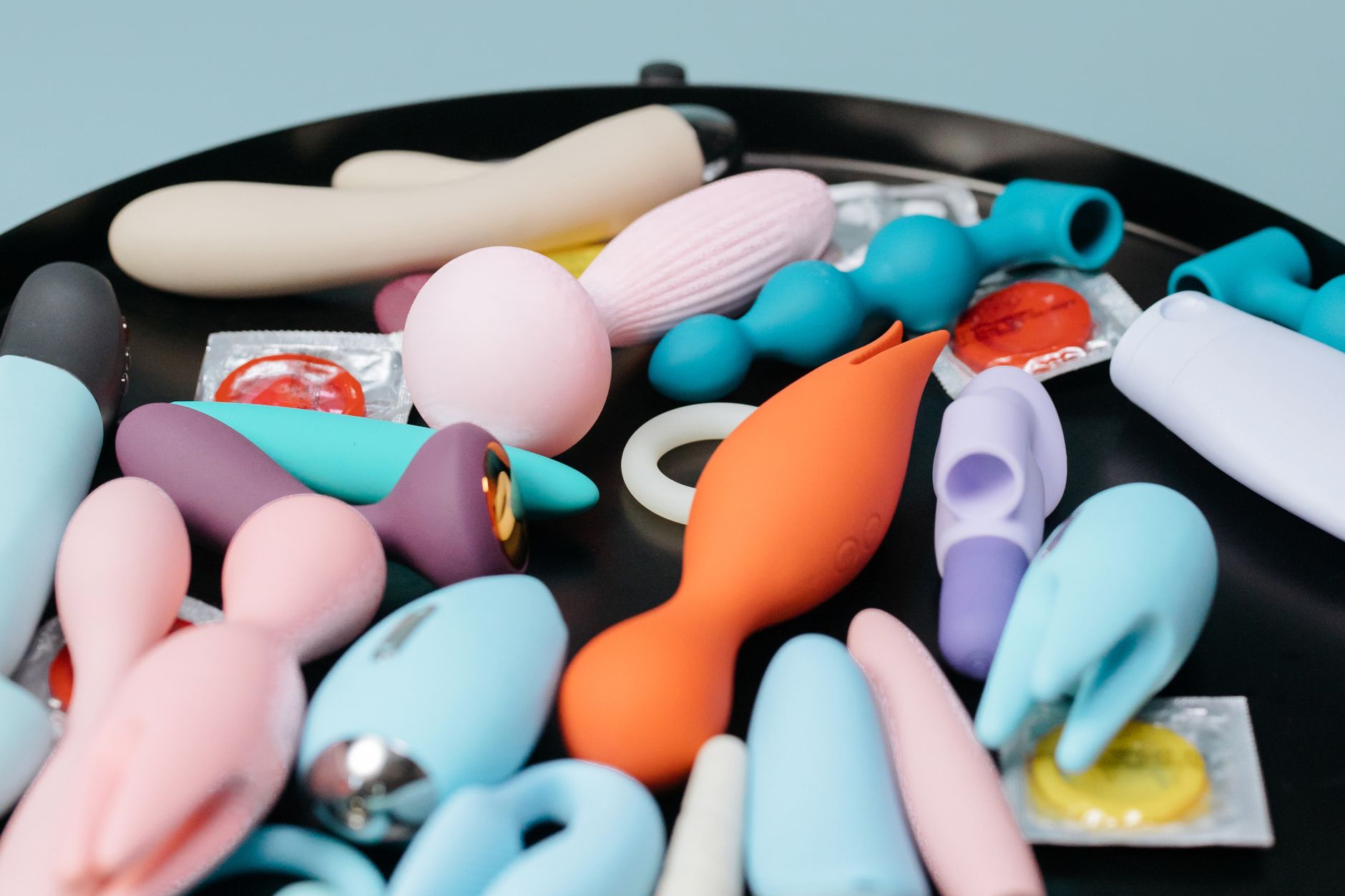 Two hands holding pink and blue silicone vibrators together against a pastel background