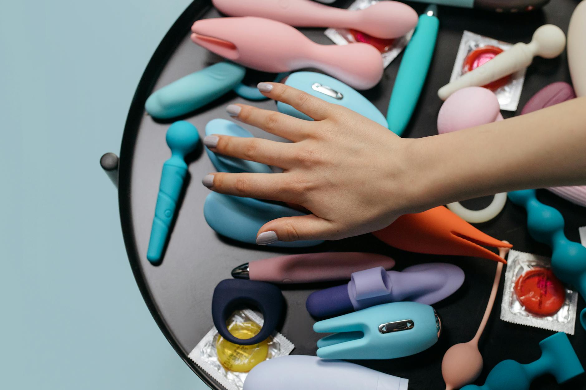 A hand reaching over a variety of colorful adult toys arranged on a table.