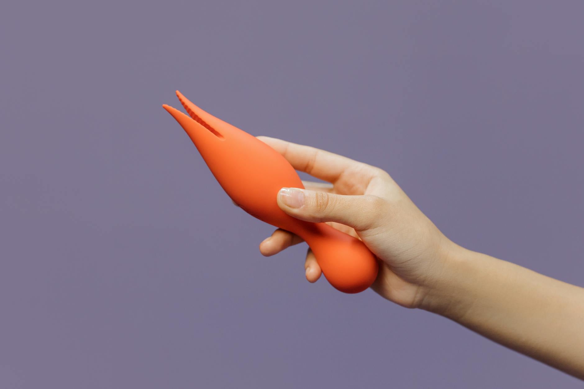 A close-up of a hand holding a bright yellow lemon vibrator against a minimalistic purple backdrop, showcasing modern sensuality.