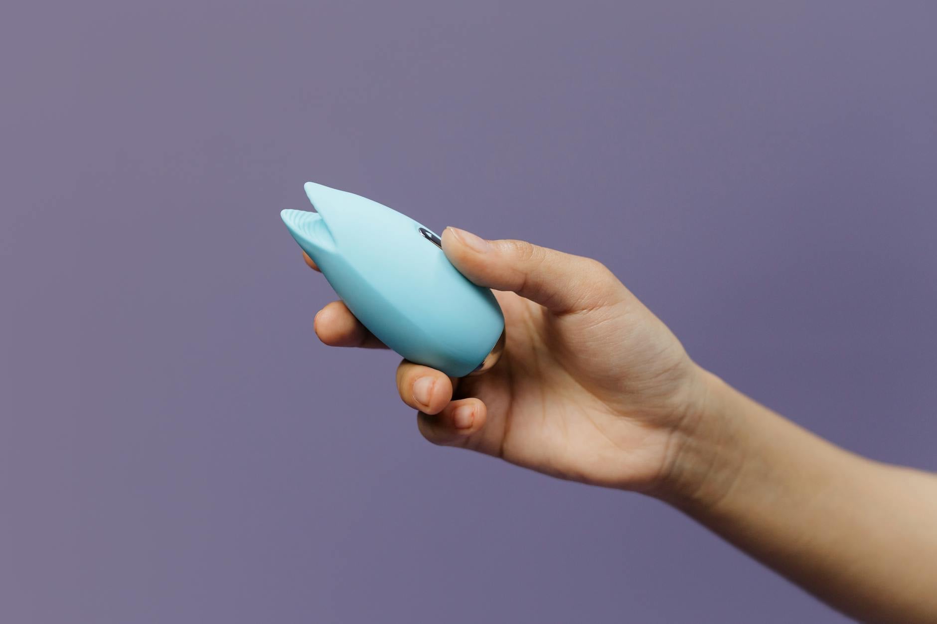 A hand holding a blue silicone vibrator against a purple background, representing self-discovery and reconnection
