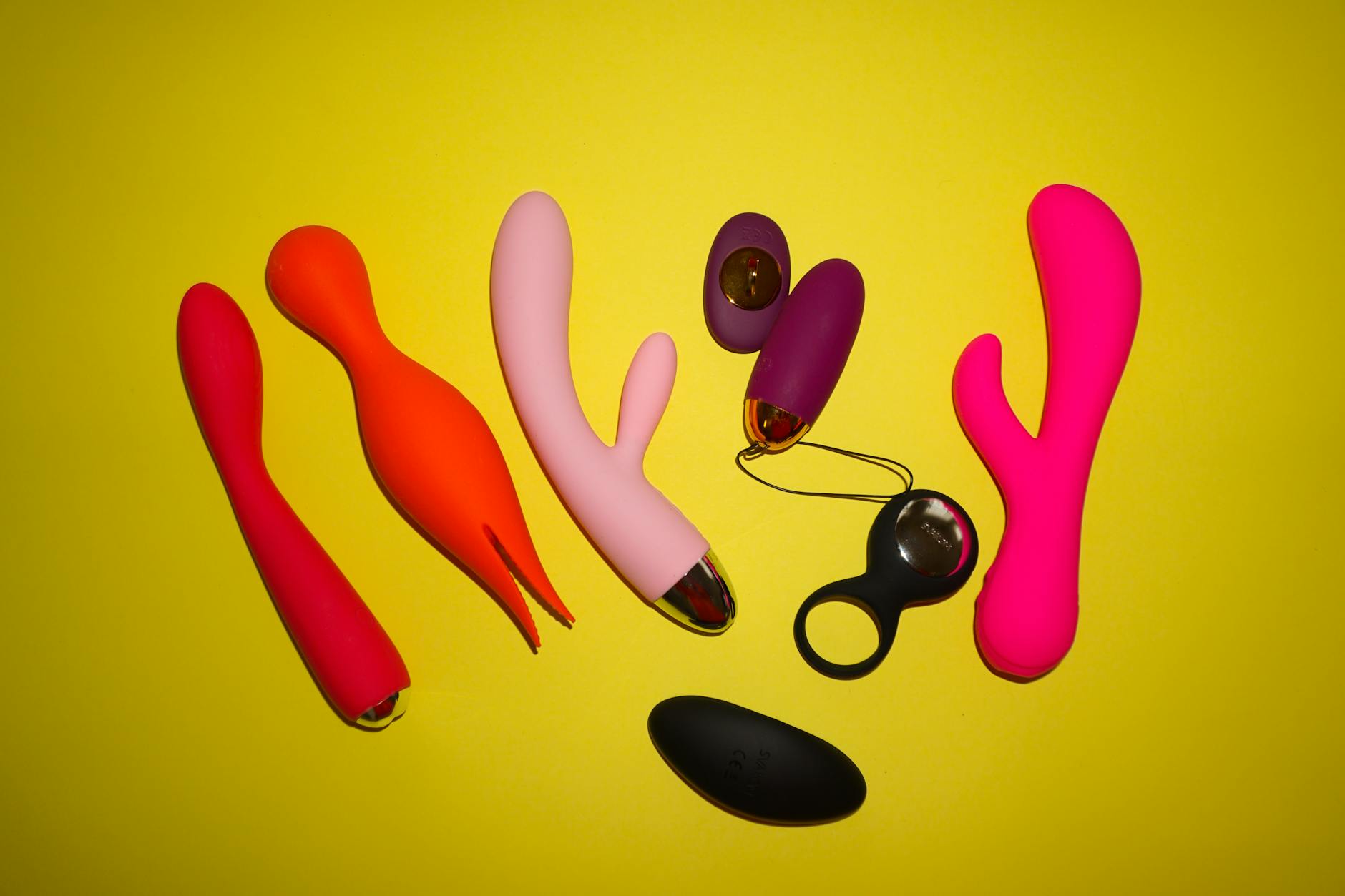 Colorful adult toys including clitoral vibrators arranged on bright yellow background